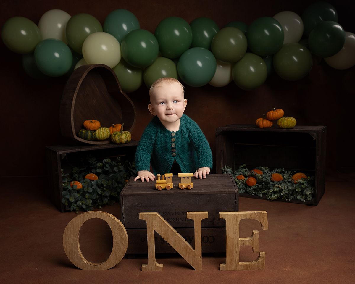A baby celebrating first birthday with balloons, pumpkins, wooden crates, and