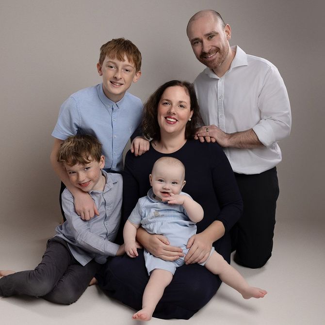 Family portrait: mother, father, and three sons. They are in a studio with neutral background, all smiling.