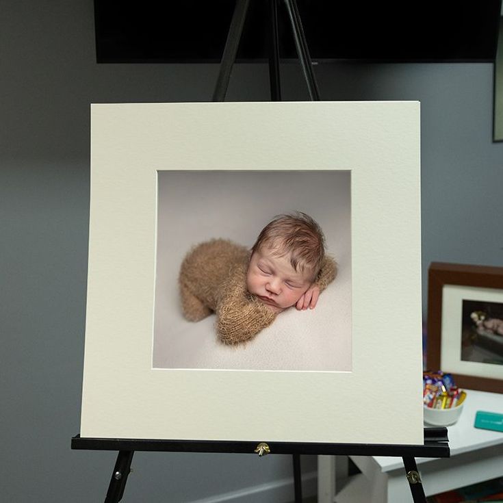 Newborn baby in brown outfit, framed on an easel.