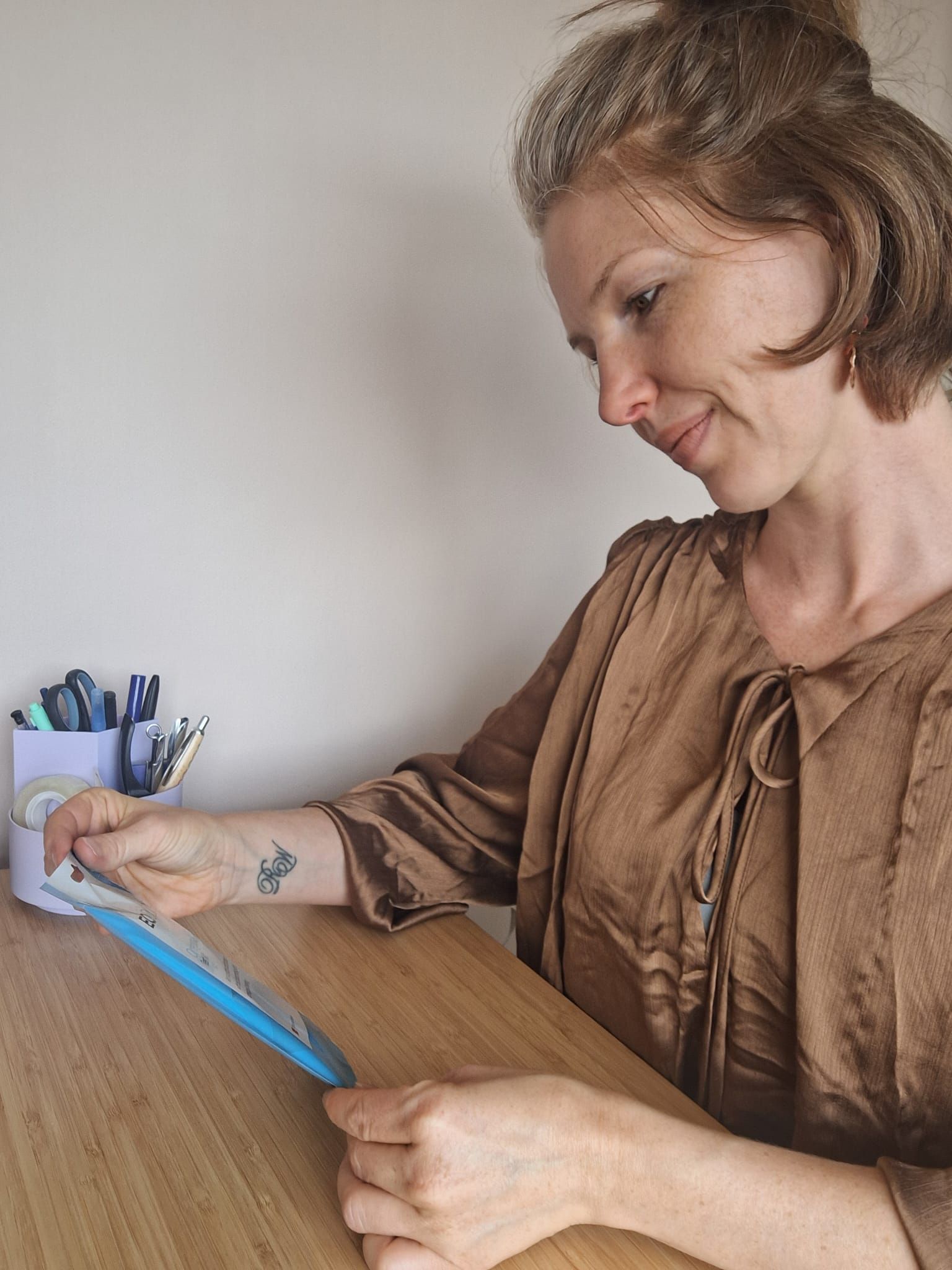 Vrouw meet stof op met een blauwe liniaal aan een bureau, met naaigerei binnen handbereik.