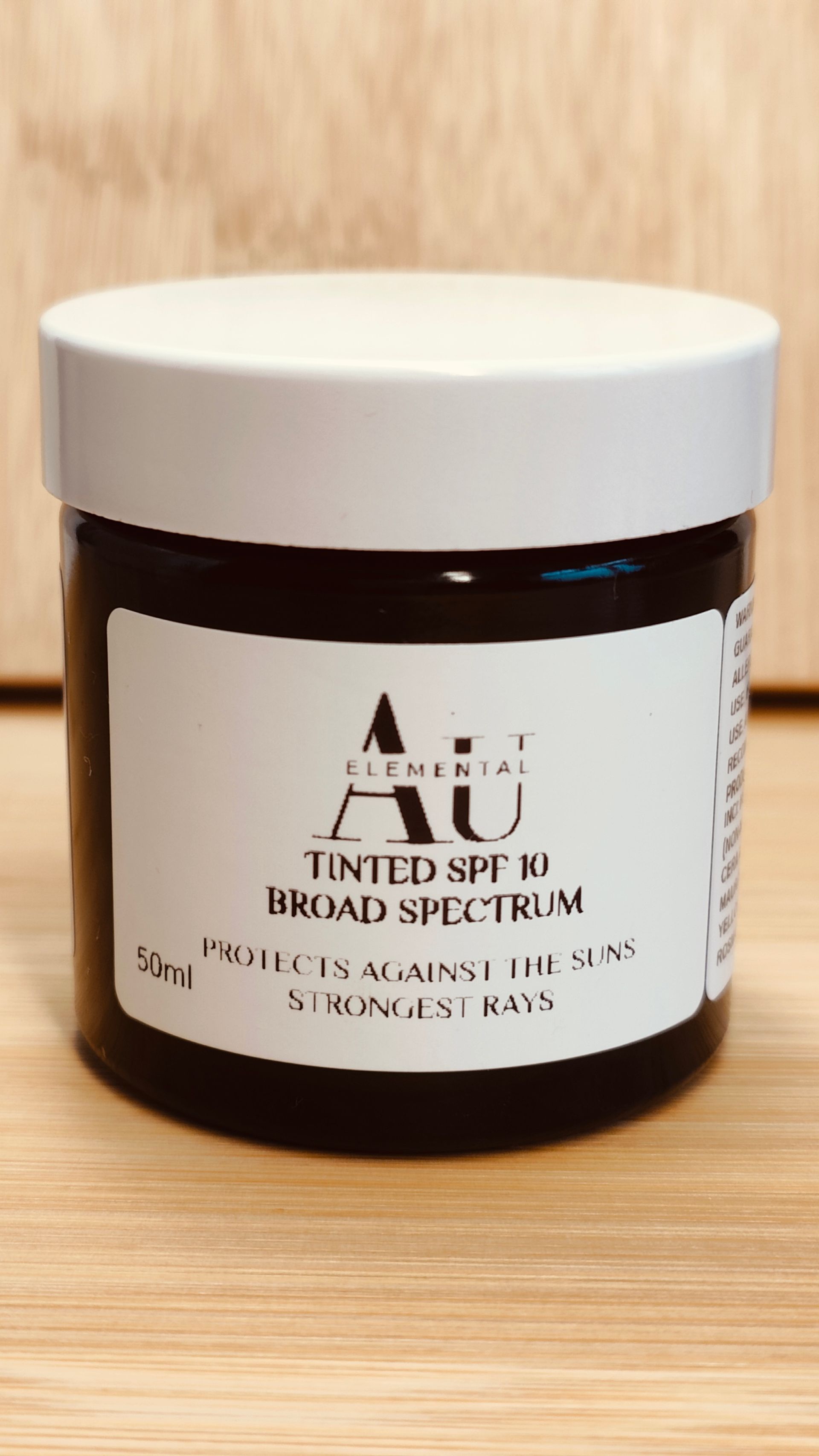 Dark jar of Au Elemental tinted SPF 30 broad spectrum sunscreen with white label and lid.