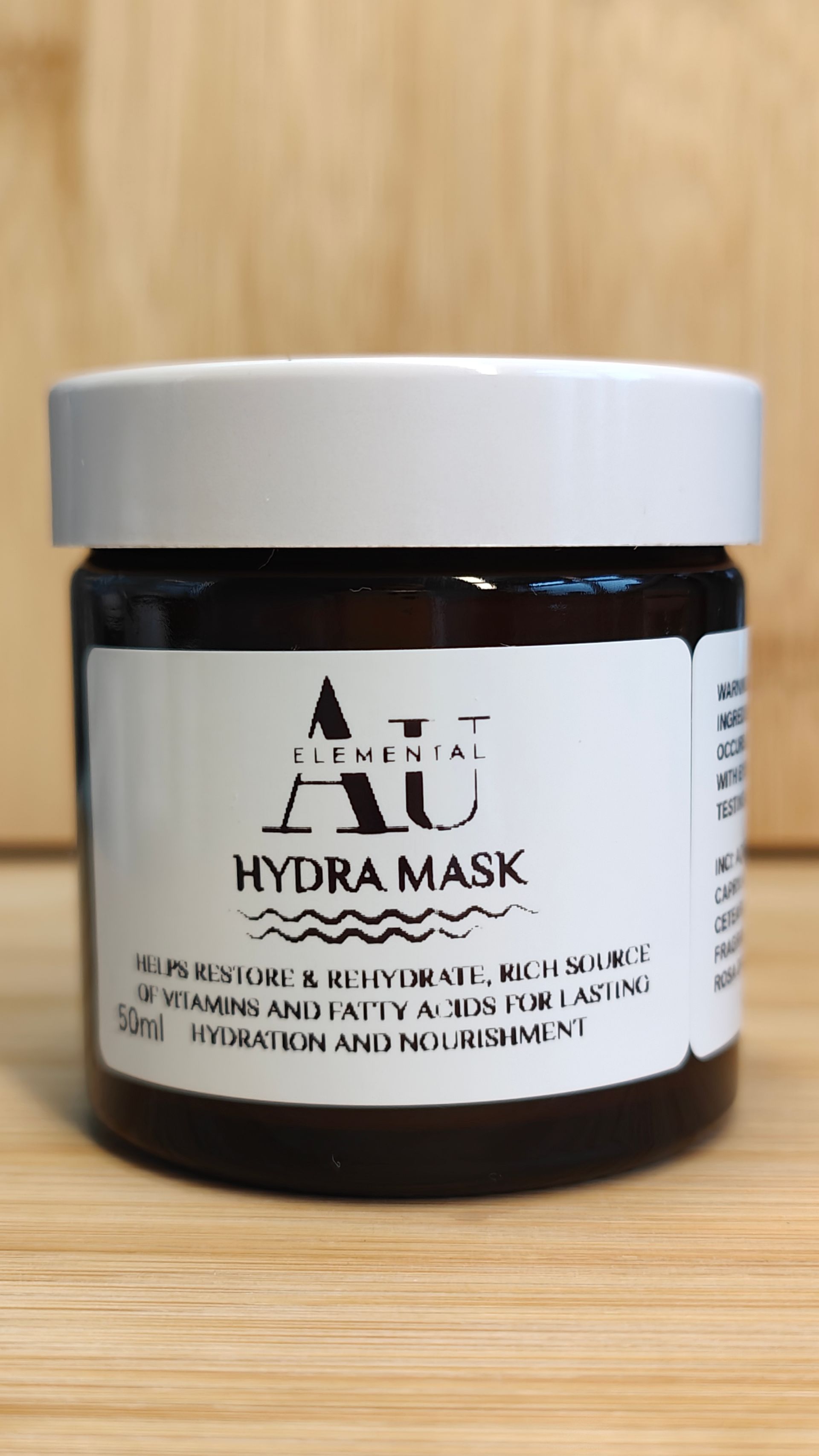 Jar of AU Elemental Hydra Mask with a white label, on a wooden surface.