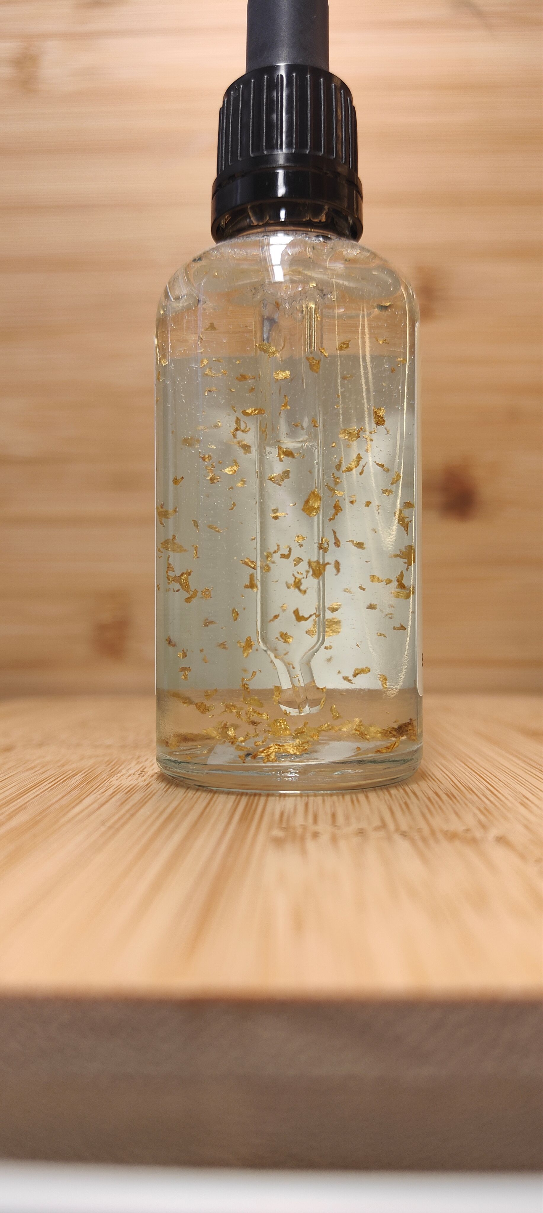 Clear glass bottle with dropper, white label, on a wooden surface.