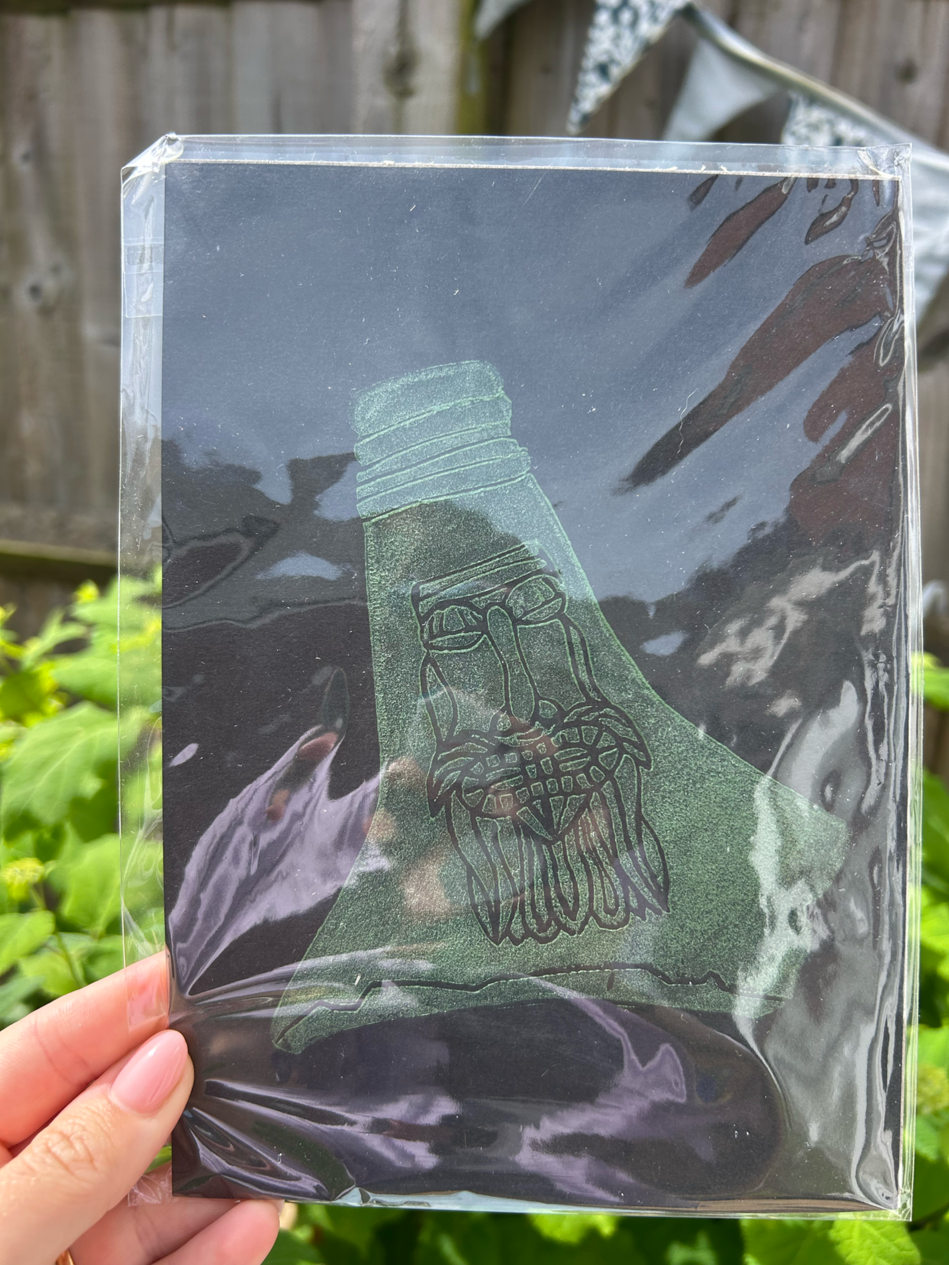 Shrink-wrapped white lino print of bellarmine jug. Green paint on white paper A5 size.