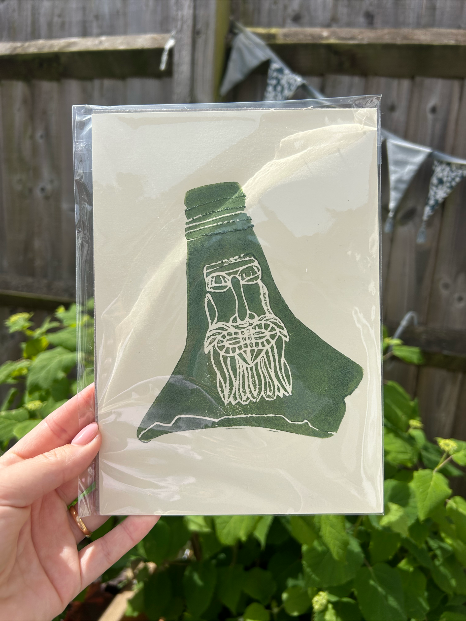 Shrink-wrapped white lino print of bellarmine jug. Green paint on white paper A5 size.