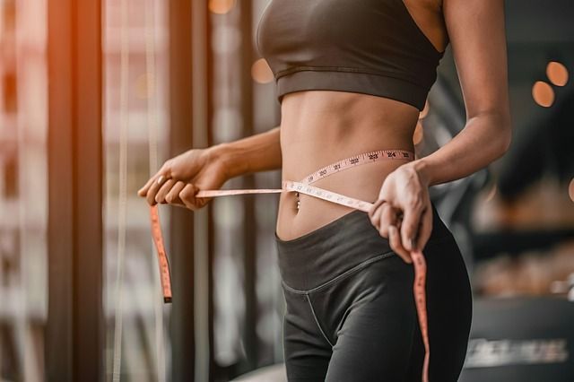 Person measuring waist with a tape measure in a gym setting