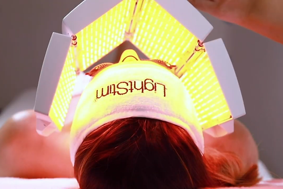 A woman is getting a light treatment on her face.