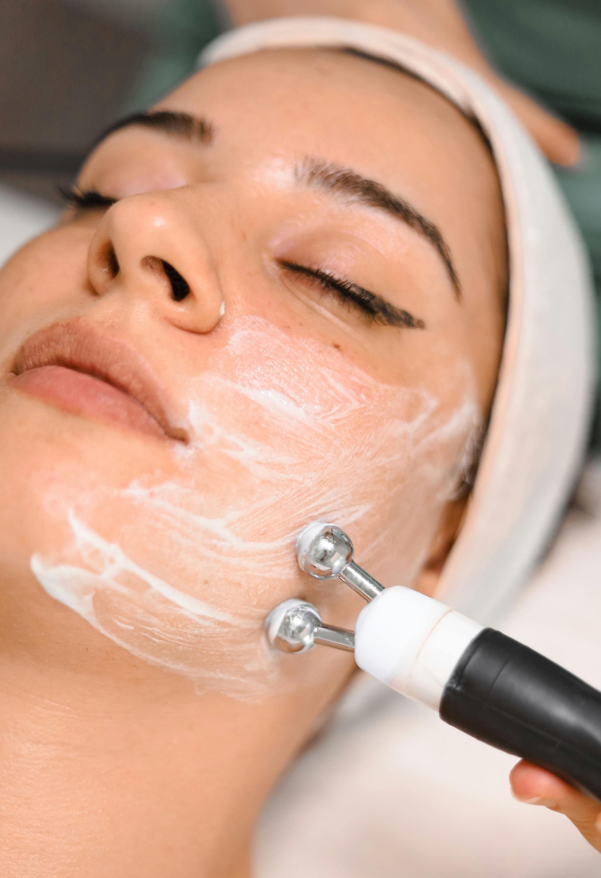 Woman receiving facial treatment with tool applying cream.