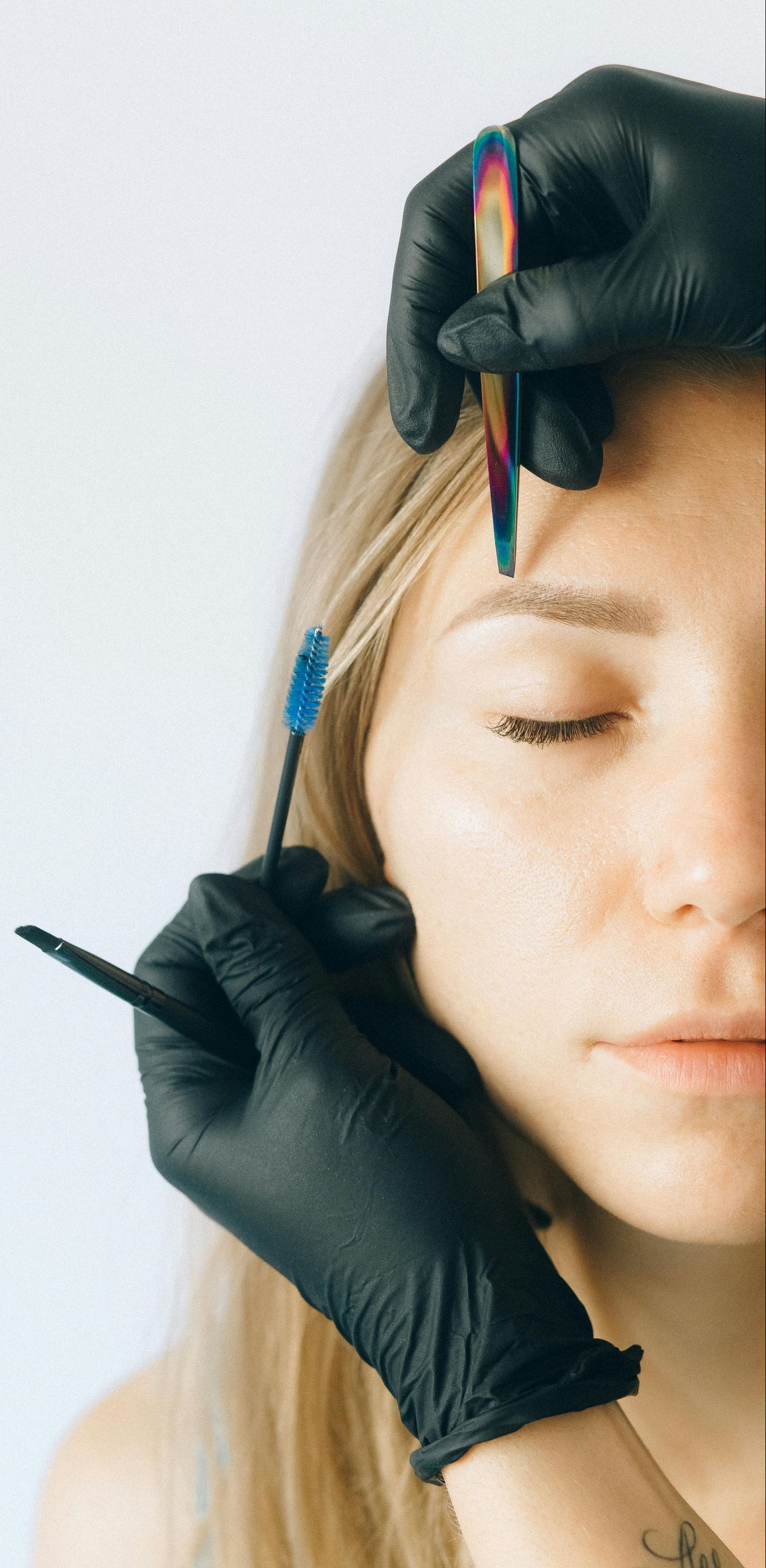 A woman having her eyebrows plucked with tweezers and brushed with a spoolie, in a beauty treatment.