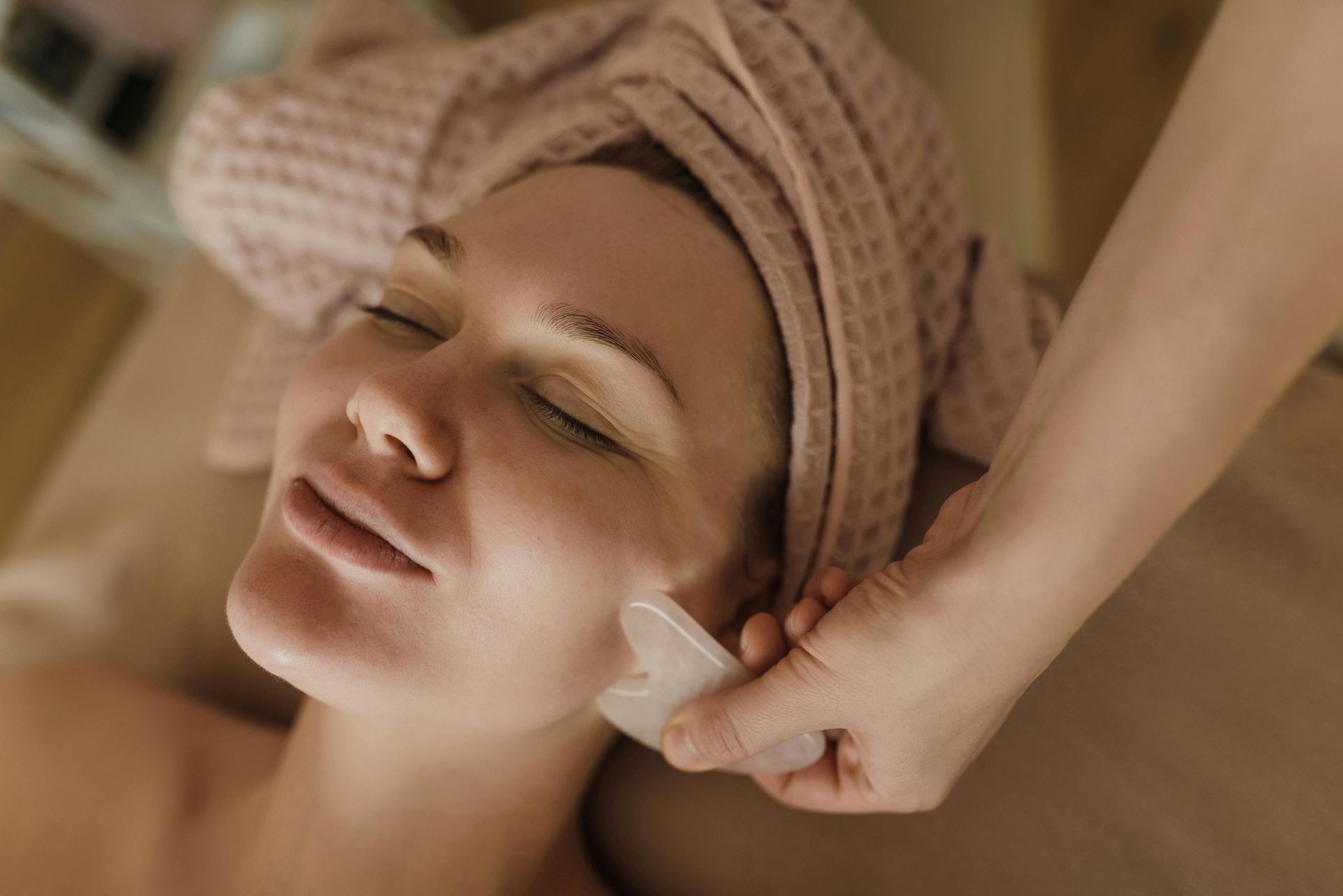 Woman receiving a facial massage with a gua sha tool in a spa setting.