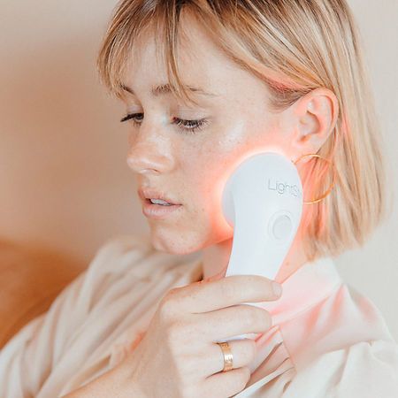 A woman is using a red light device on her face.