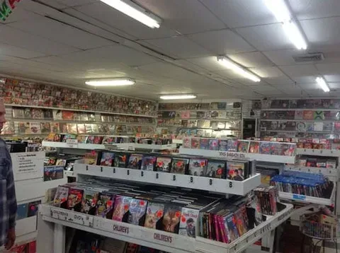 A man is standing in a store filled with lots of dvds.