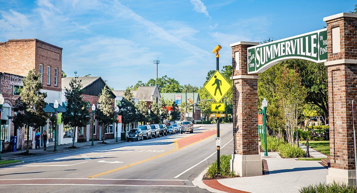 Summerville welcome sign over a street lined with shops and parked cars under a blue sky.