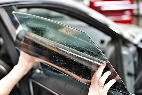 Hands peeling tinted film from a car window indoors