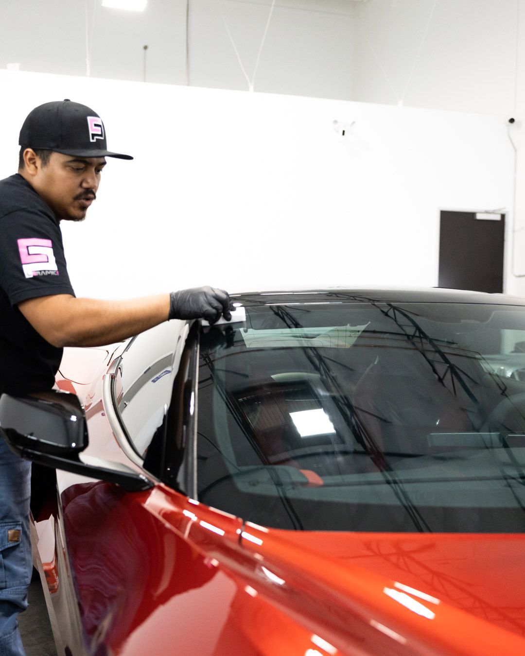 Technician wiping the windshield of a red car in a garage.