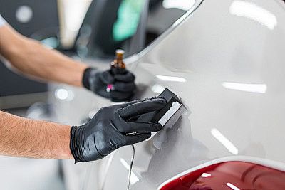 Gloved hands polishing a white car with a cloth, likely detailing the vehicle