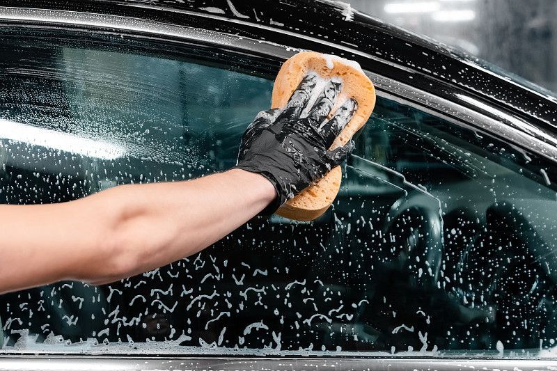 Gloved hands polishing a white car with a cloth, likely detailing the vehicle