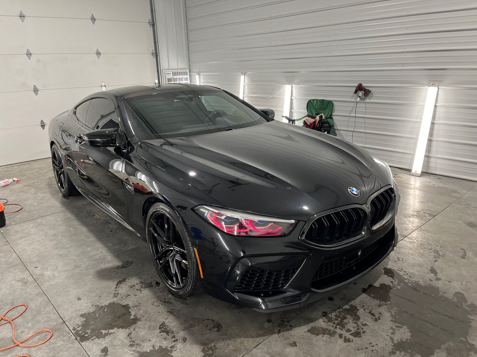Black BMW coupe in a garage, front-left view with wet floor reflections