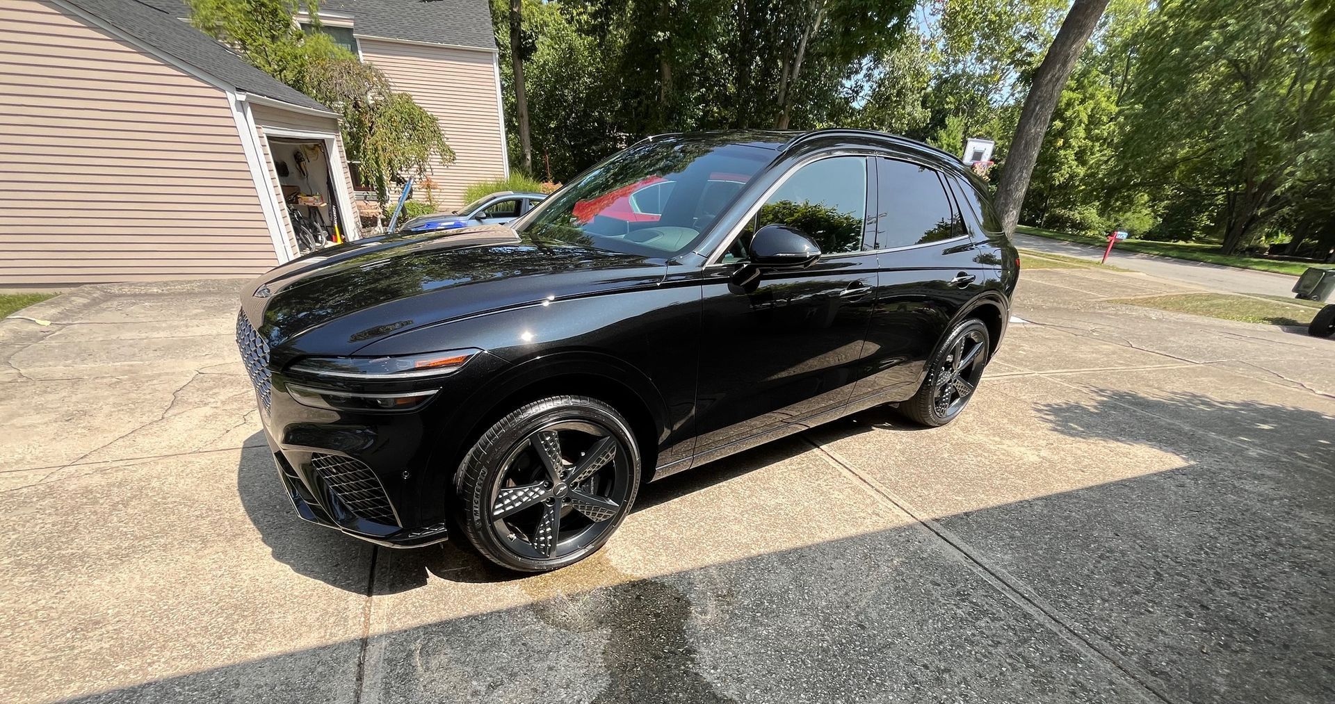 Black SUV parked on a driveway beside a house, viewed from the front-left side.