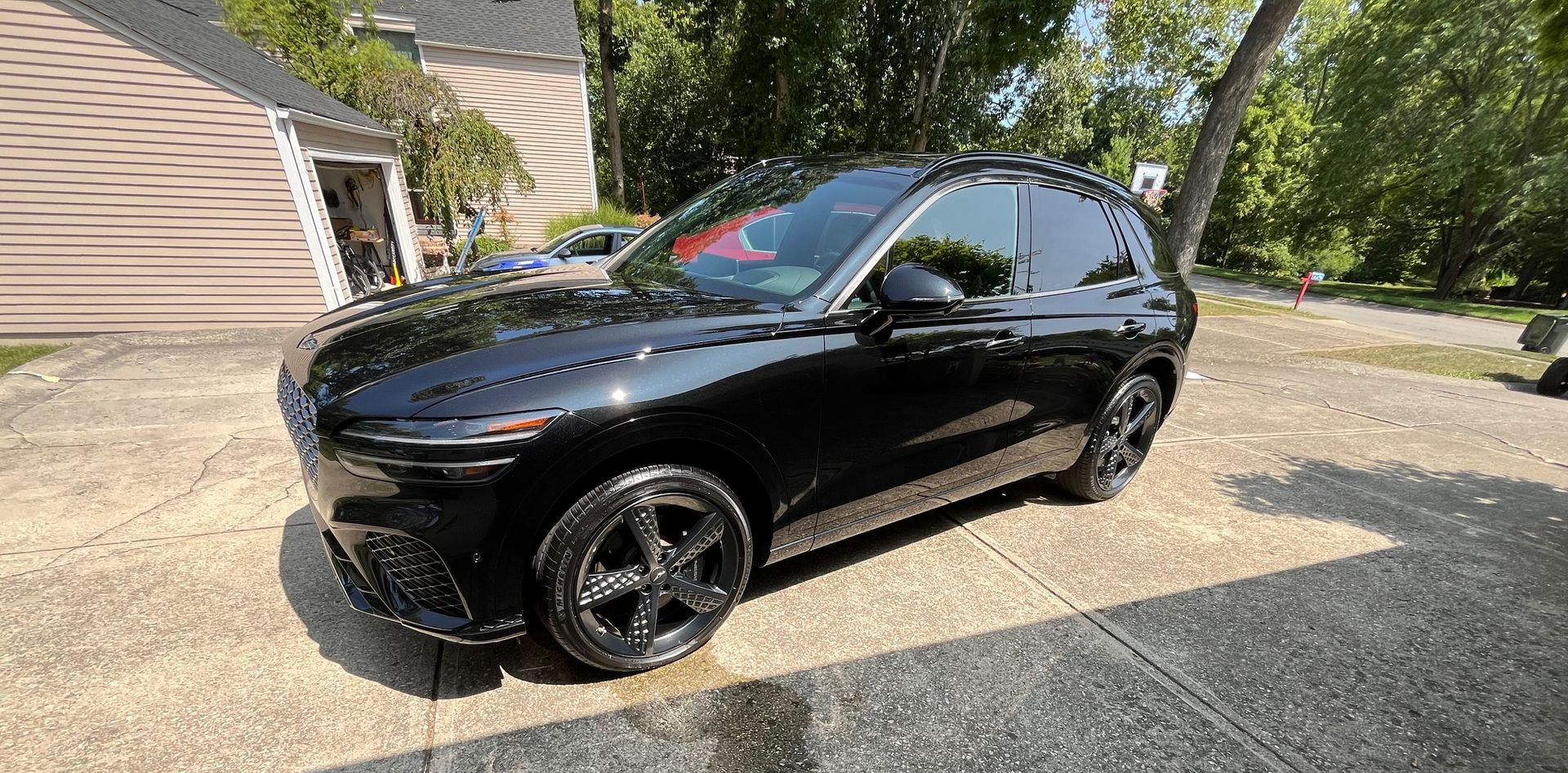 Black SUV parked on a driveway beside a house in a sunny suburban yard.