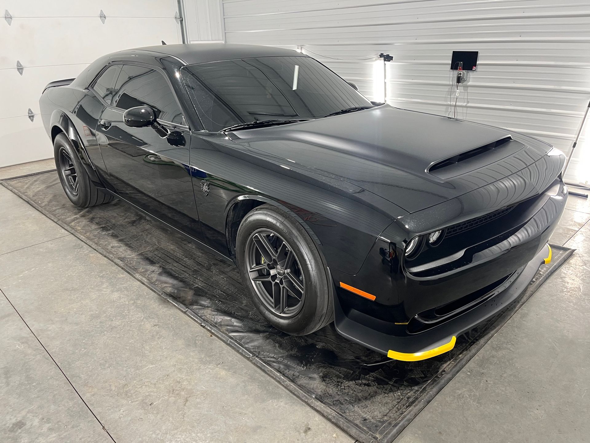 Black Dodge Challenger parked in a garage, front-left view, with yellow splitter guards.