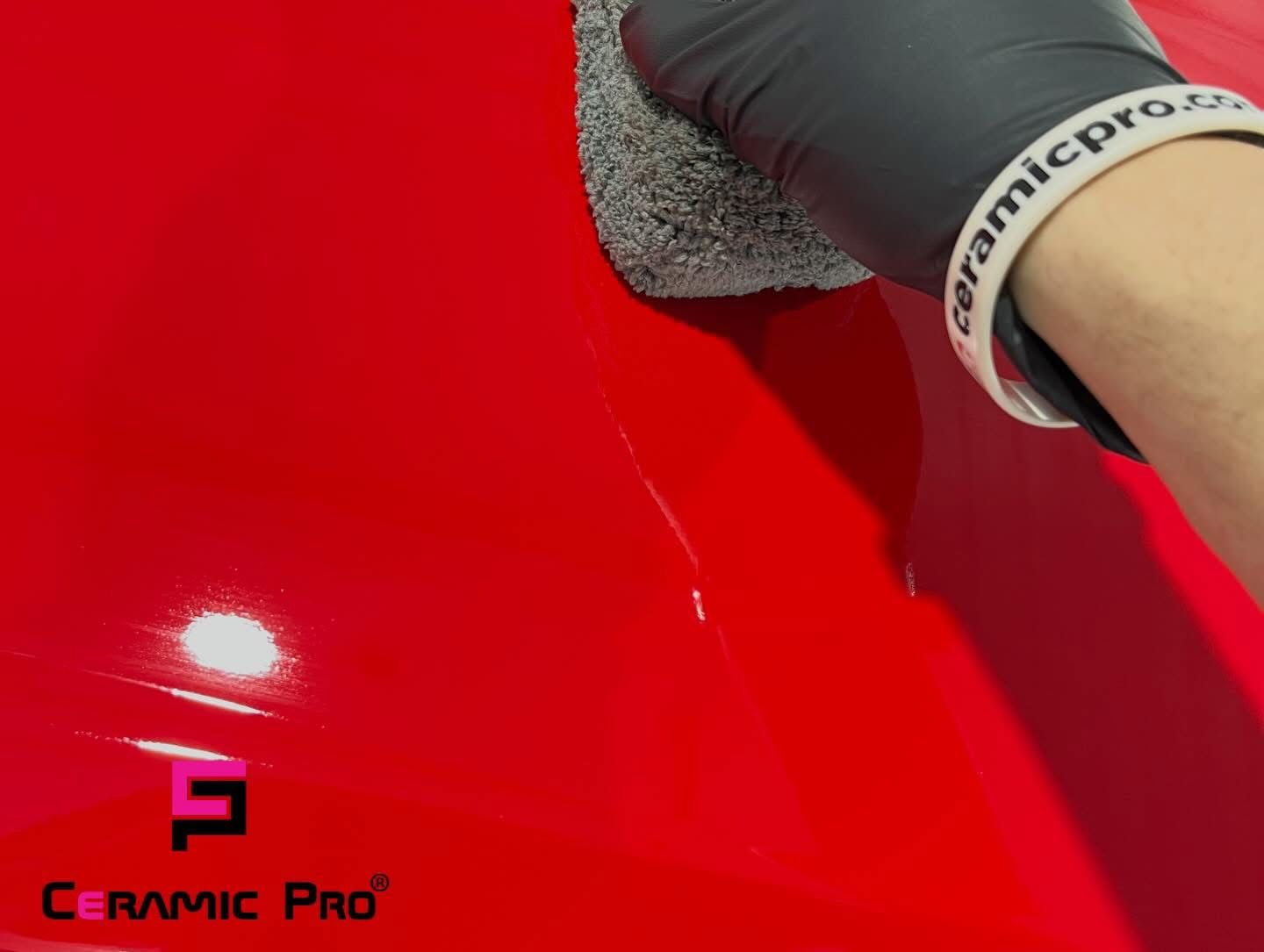 Gloved hands polishing a white car with a cloth, likely detailing the vehicle