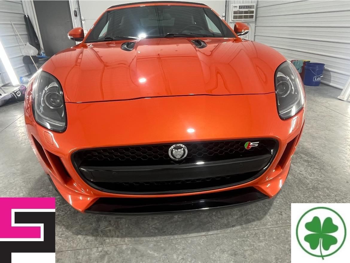 Front view of an orange Jaguar sports car parked indoors, with black grille and headlights.