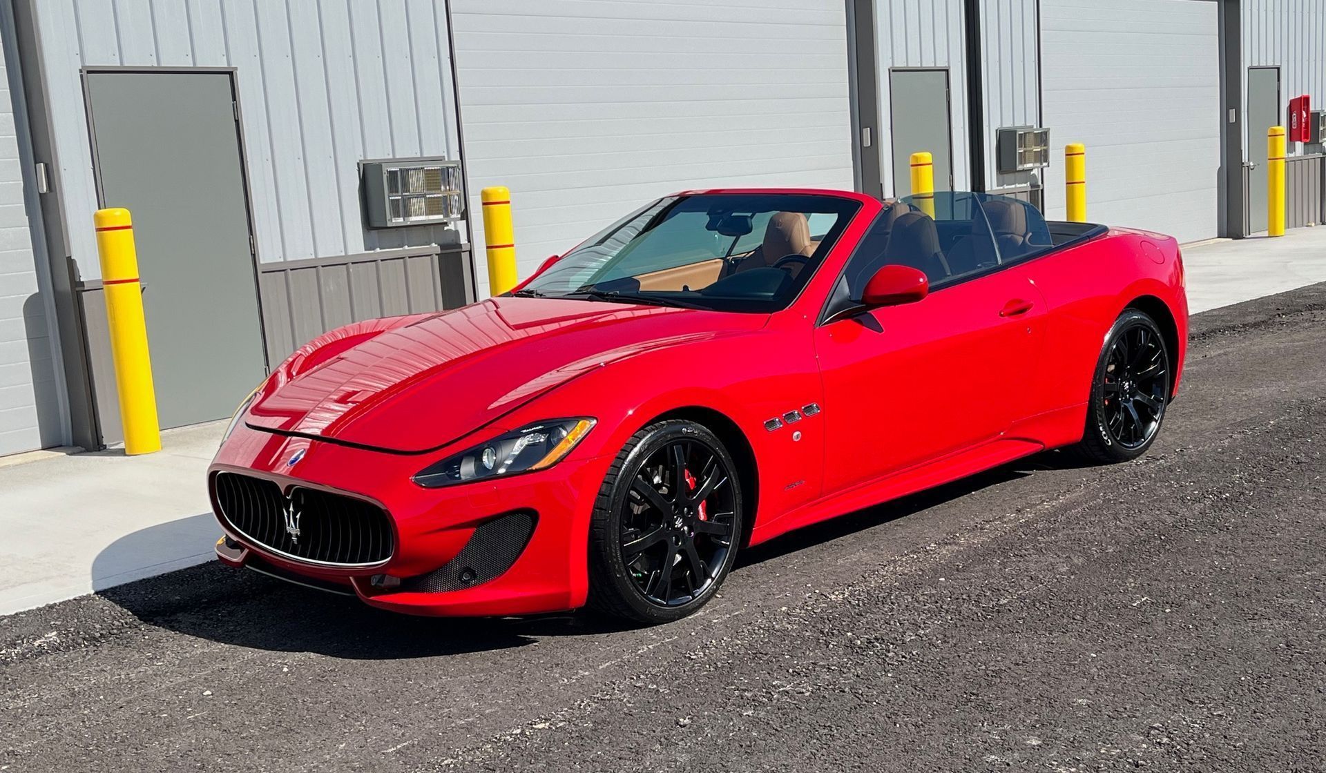 Red convertible sports car parked outside a gray industrial building.