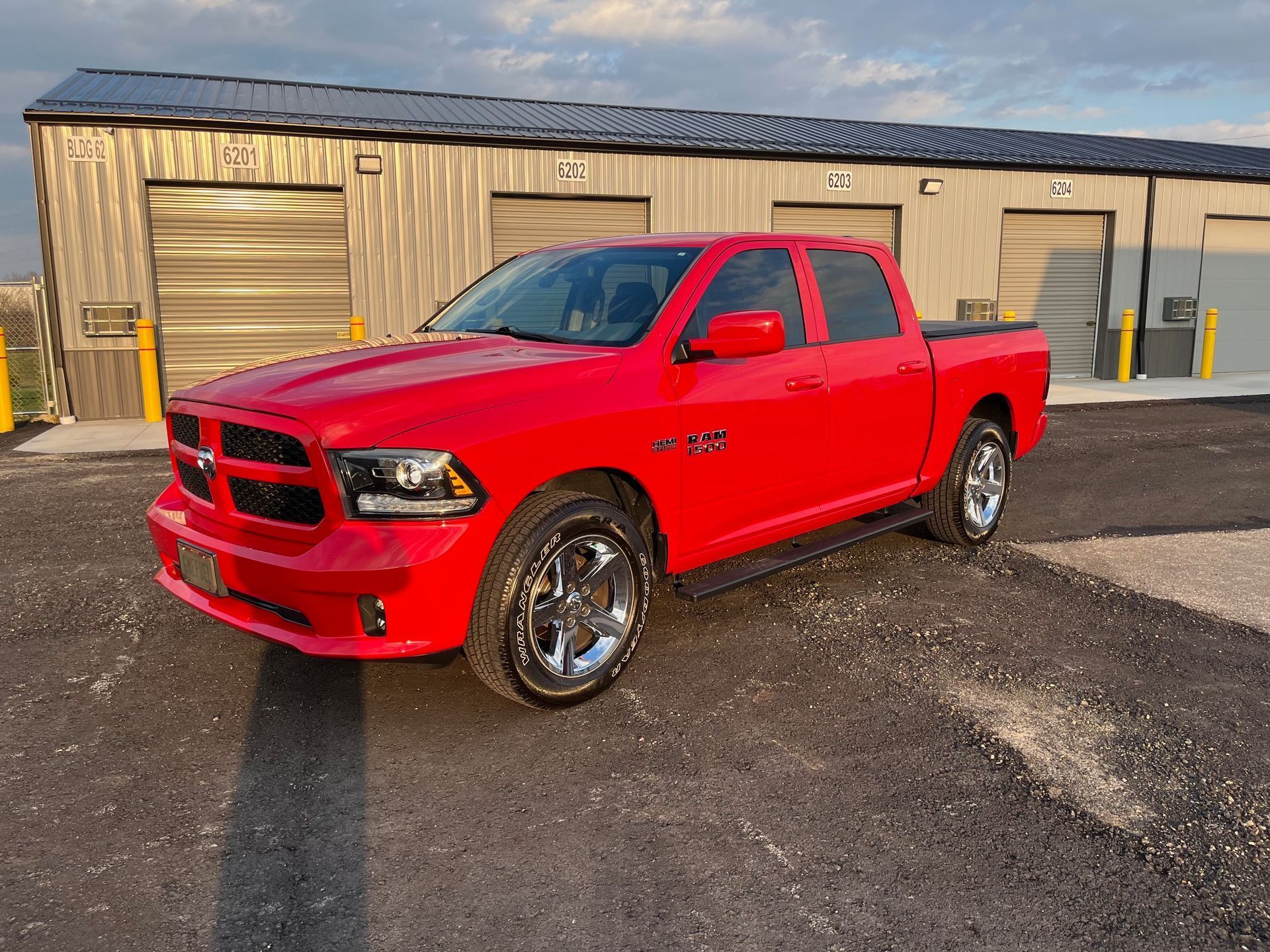 Red pickup truck parked outside a beige industrial building on a wet lot.