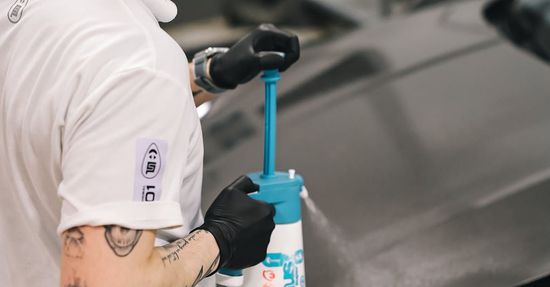 Person in black gloves uses a blue pump on a white spray bottle.
