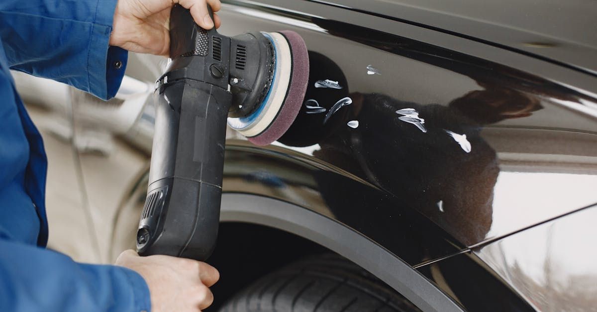 Person polishing a black car fender with a handheld buffer.