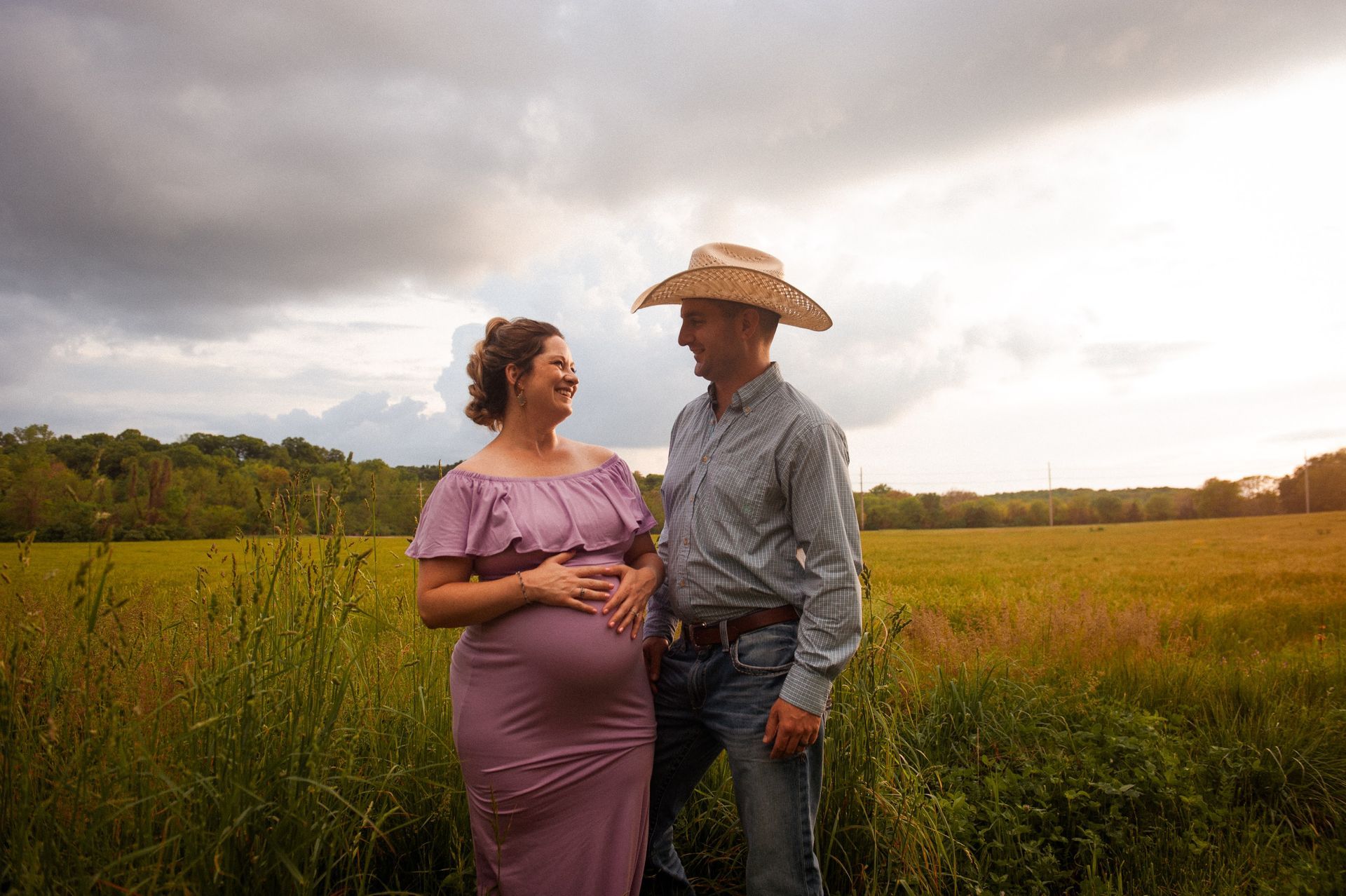 A man and a pregnant woman are standing in a field looking at each other.