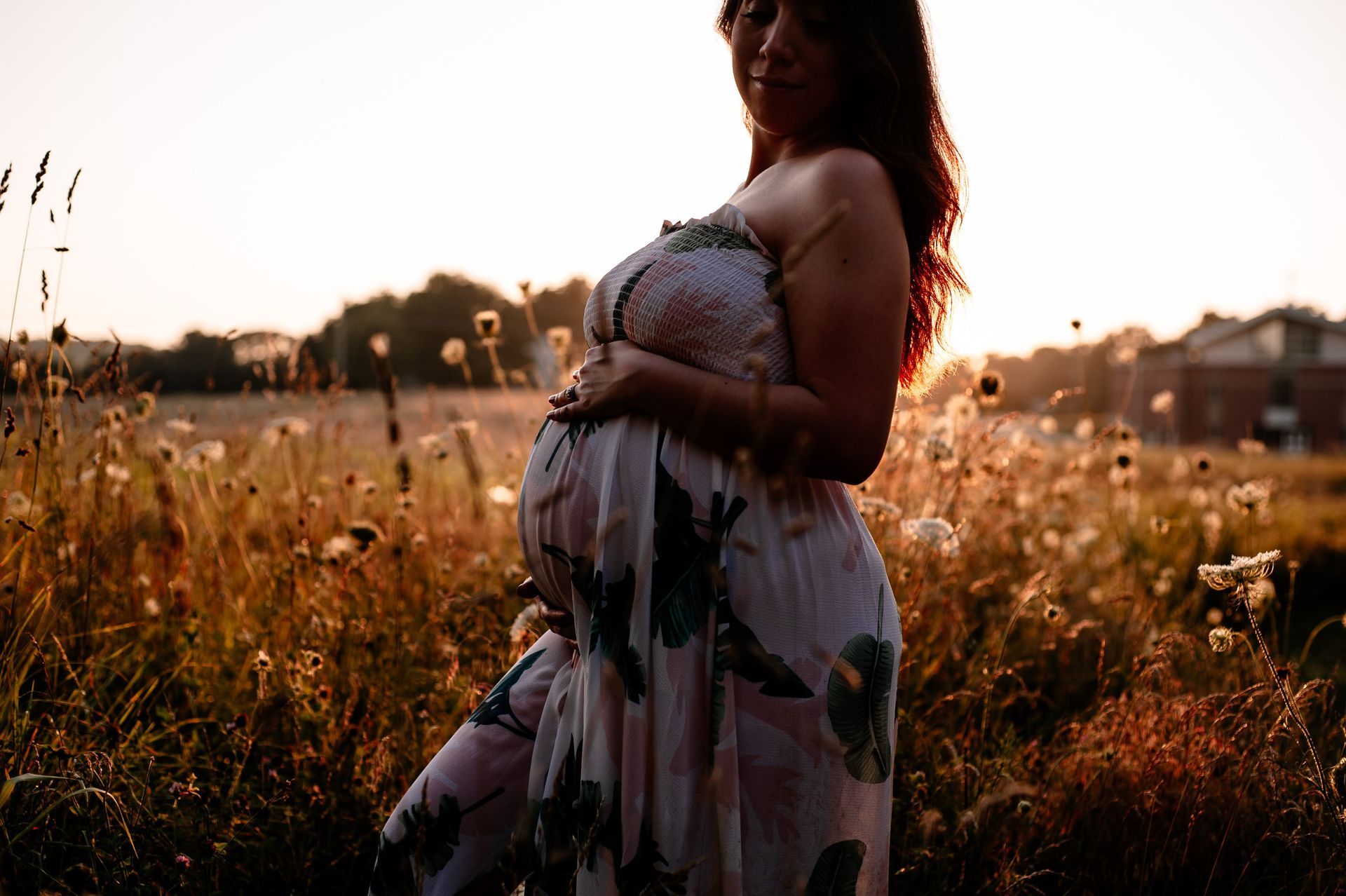A pregnant woman is standing in a field holding her belly.