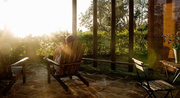 A man is sitting in a wooden chair on a porch.