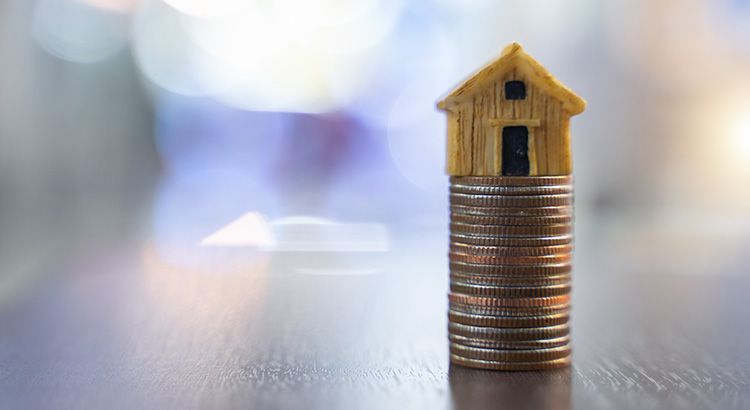 A model house is sitting on top of a stack of coins.