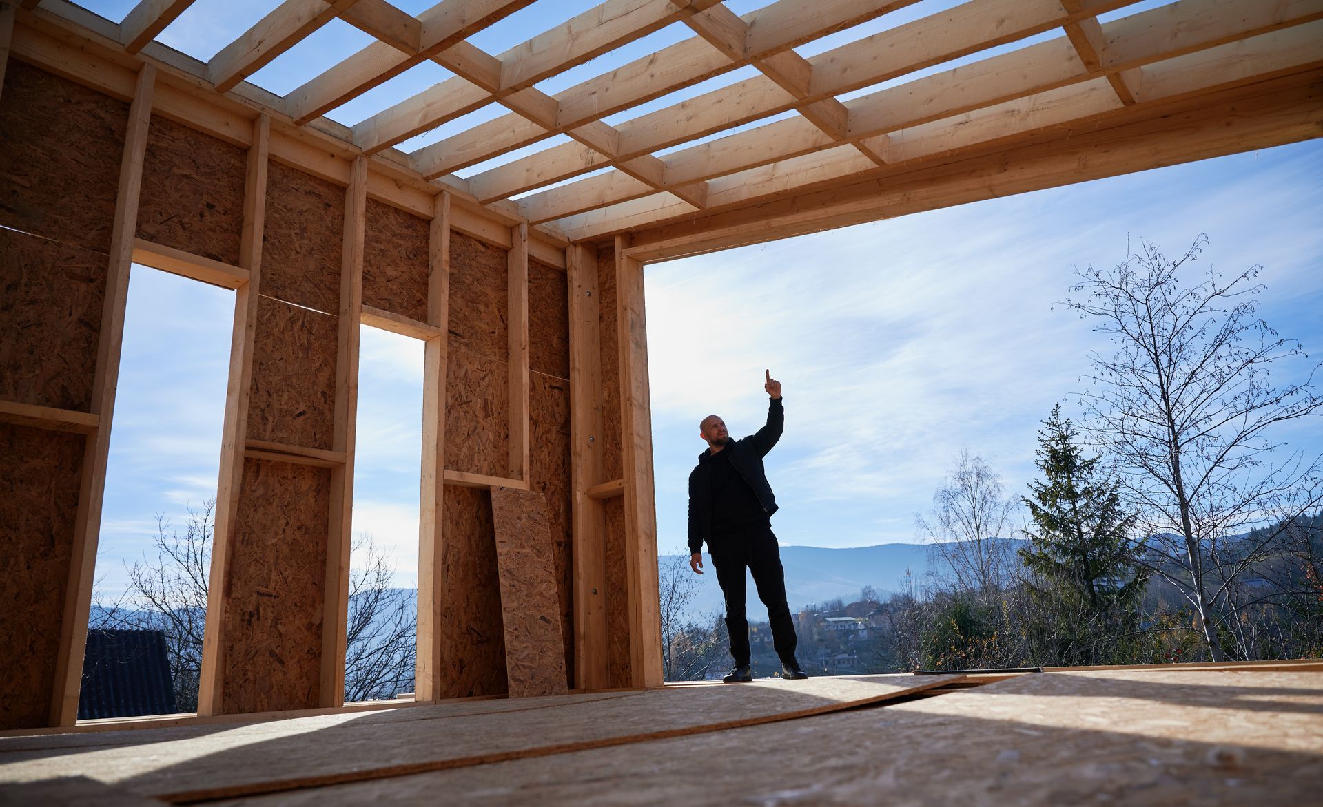 A man is standing in a wooden house under construction.