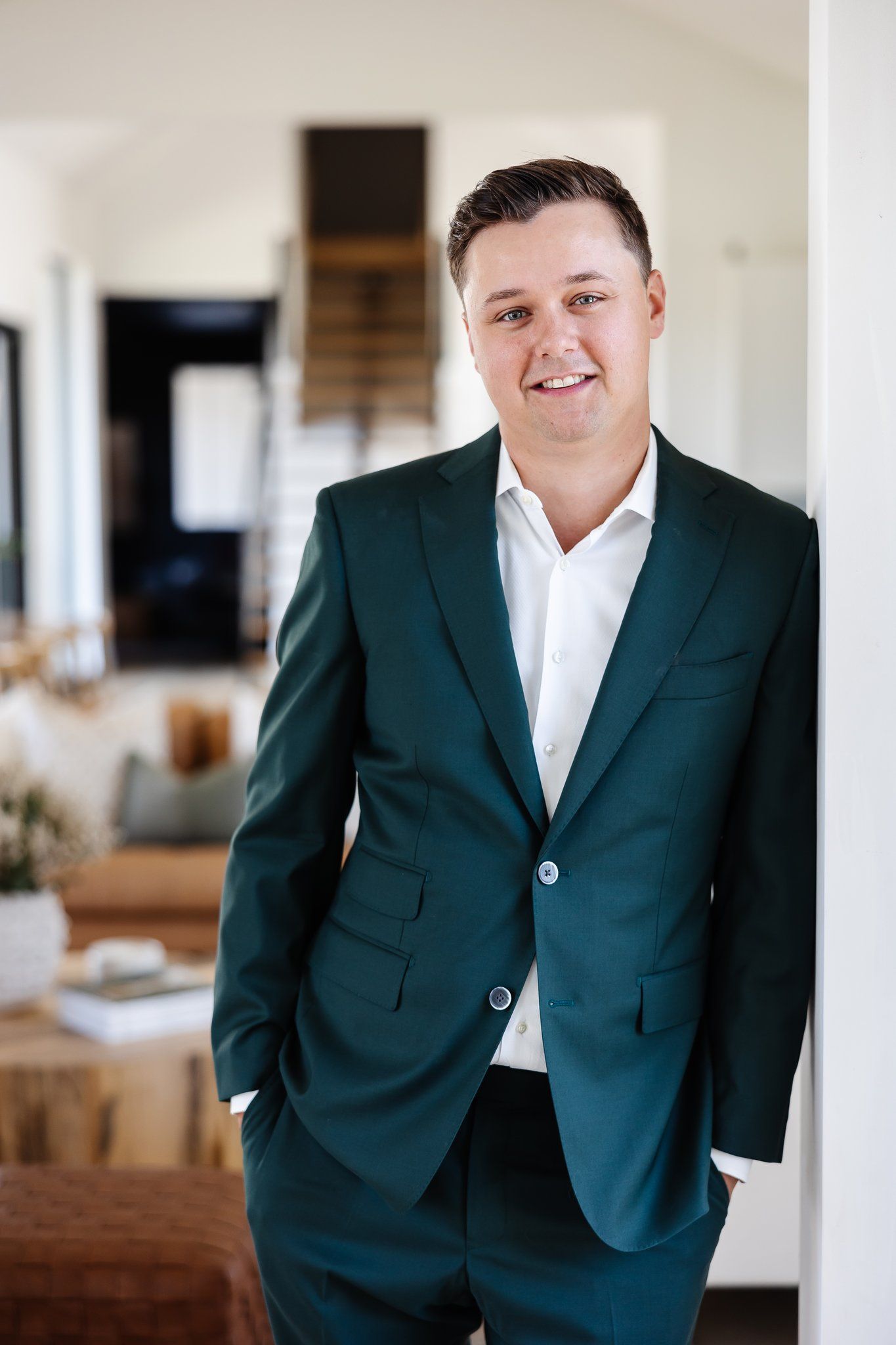 A man in a green suit and white shirt is leaning against a wall.