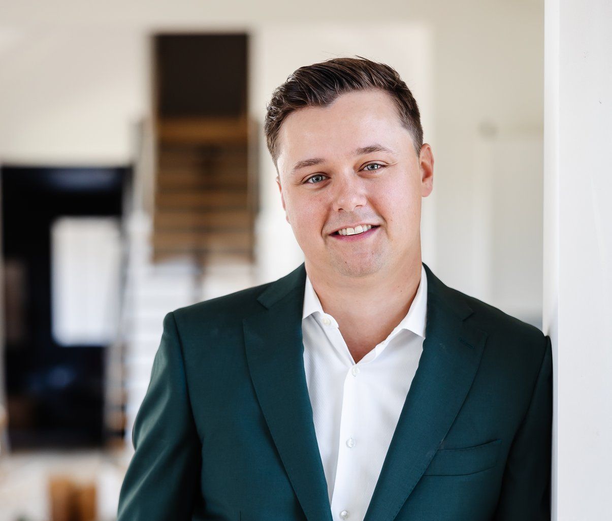 A man in a green suit and white shirt is leaning against a wall.
