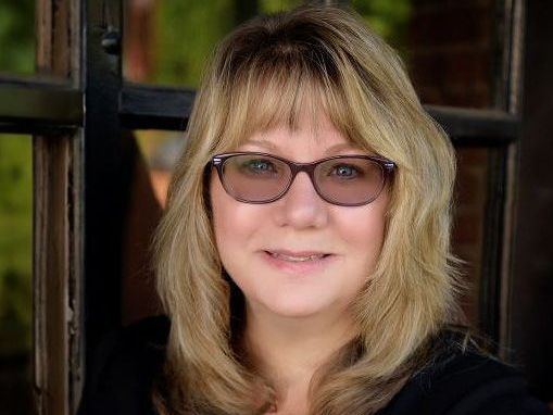 A woman wearing glasses is standing in front of a window.