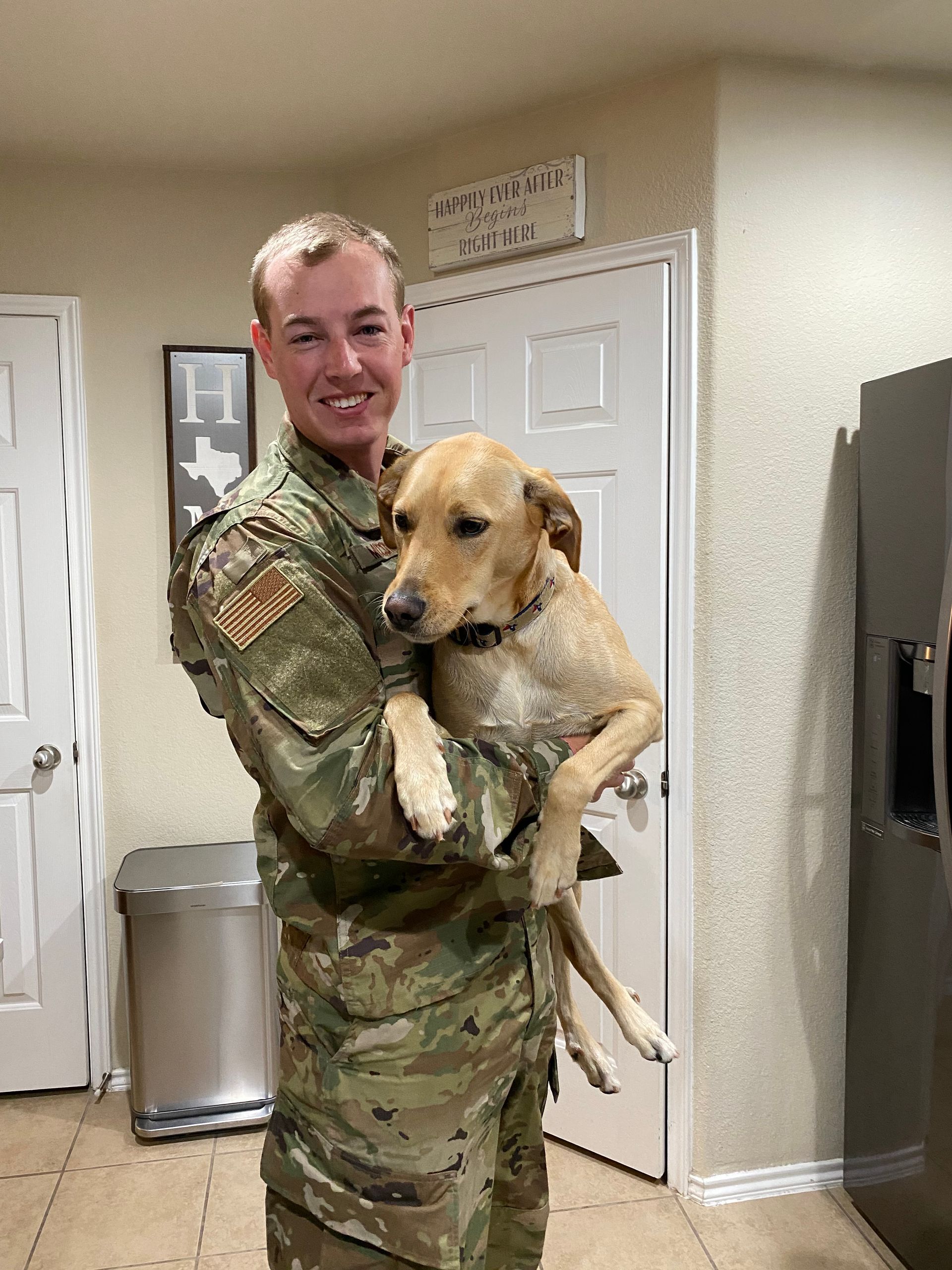 A man in a military uniform is holding a dog in his arms.