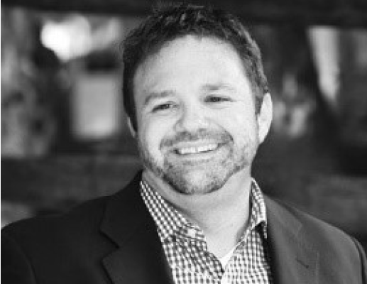 A man in a suit and plaid shirt is smiling in a black and white photo.