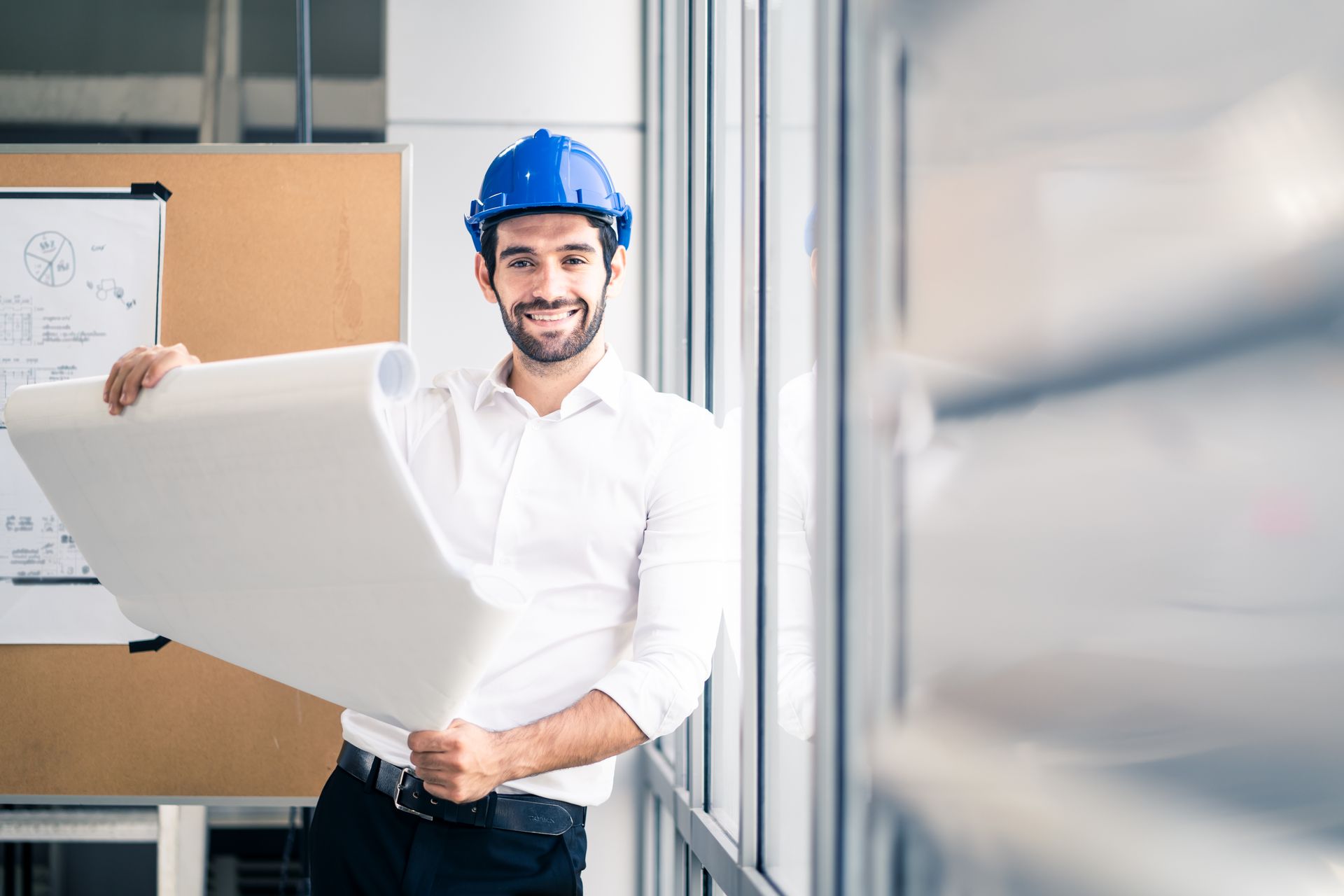 A man wearing a hard hat is holding a blueprint.