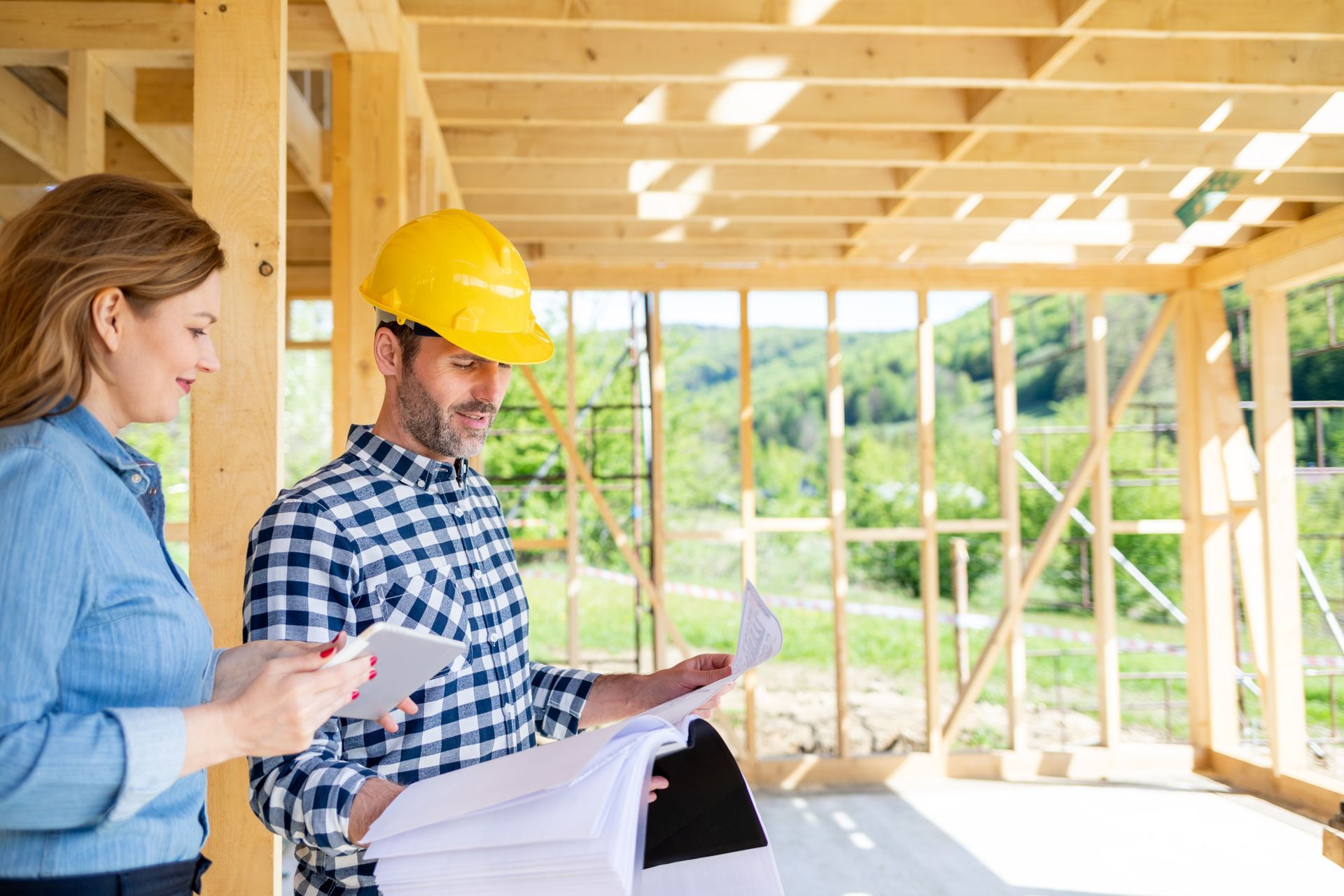 A man and a woman are looking at a blueprint at a construction site.