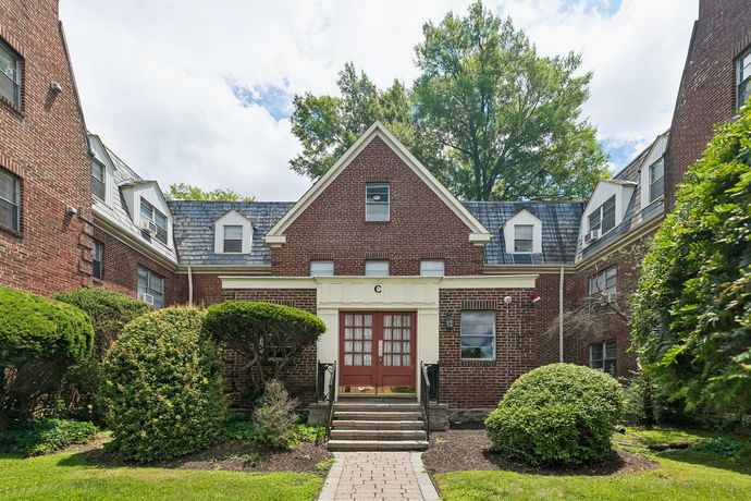 Red brick apartment building with white dormers, green lawn, and blue sky.