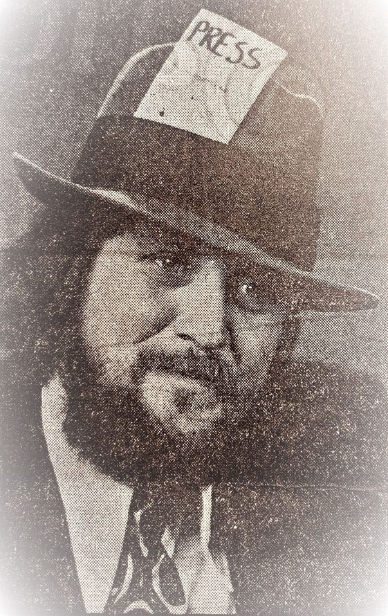 A man with a beard is wearing a hat with a piece of paper on it.