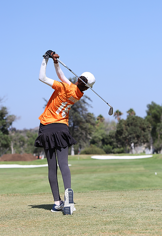 Golfer in orange shirt swinging a club on a sunny golf course