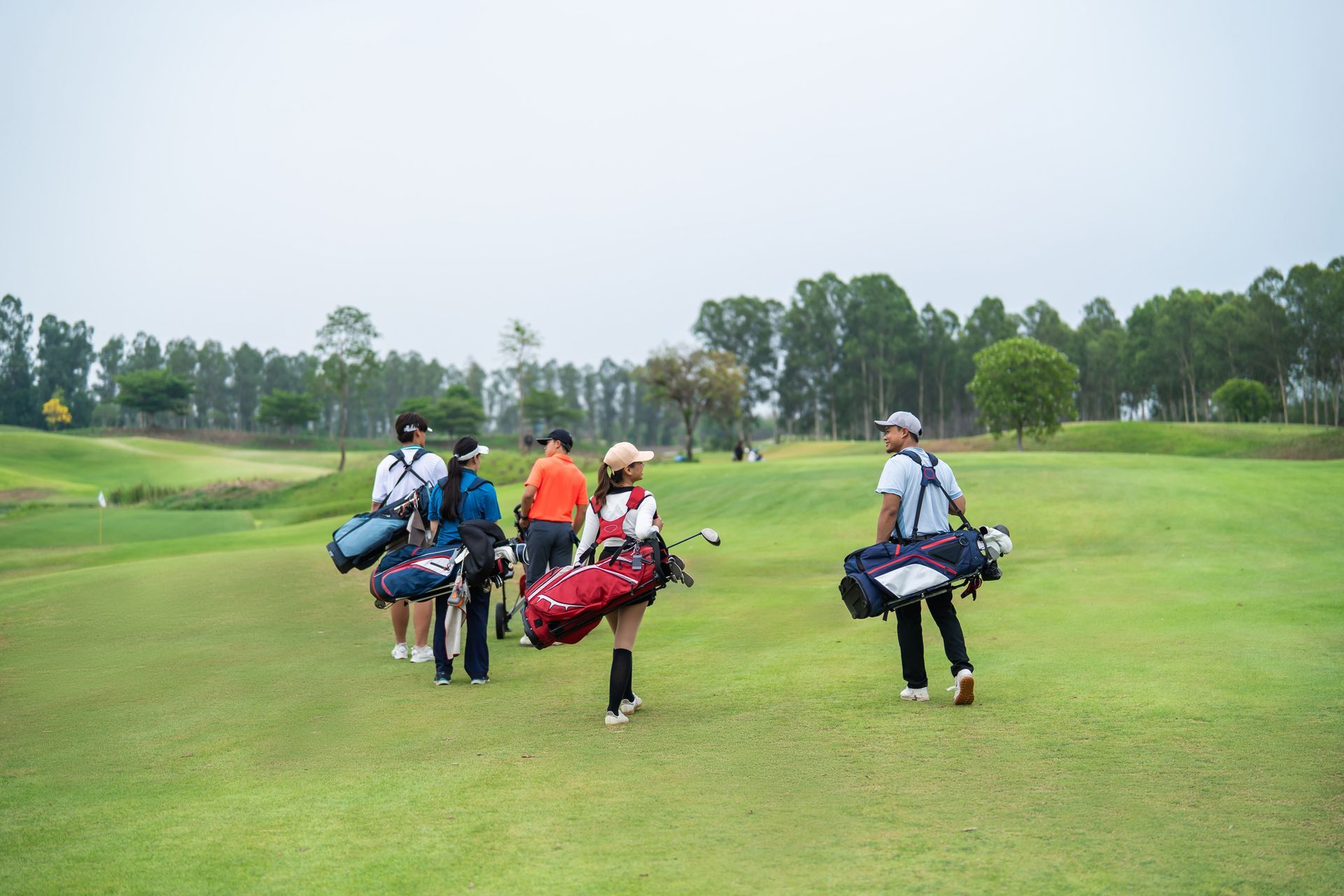 Four golfers walking across a green fairway with golf bags on a cloudy day