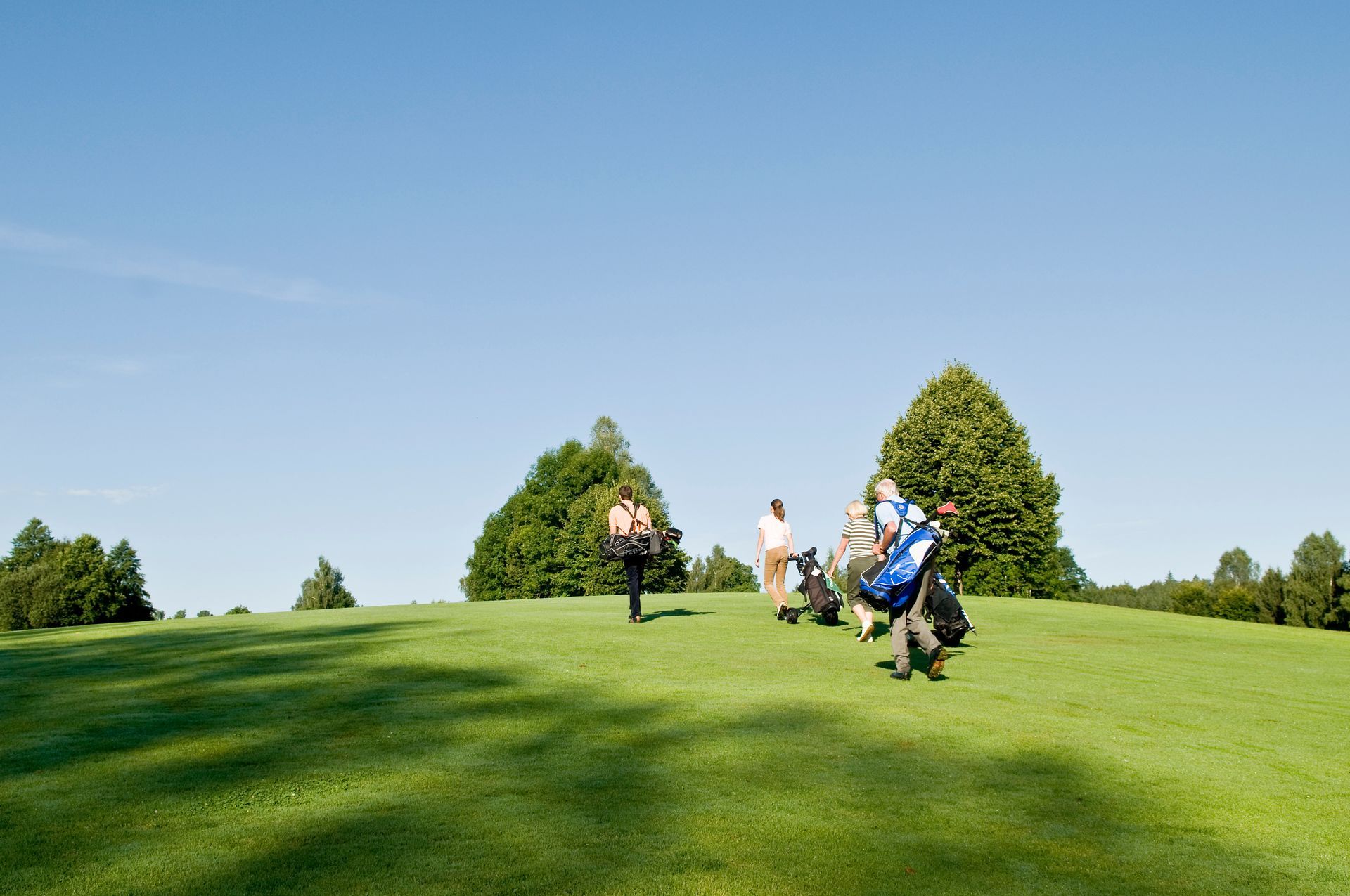 Golfers walking across a bright green course under a clear blue sky
