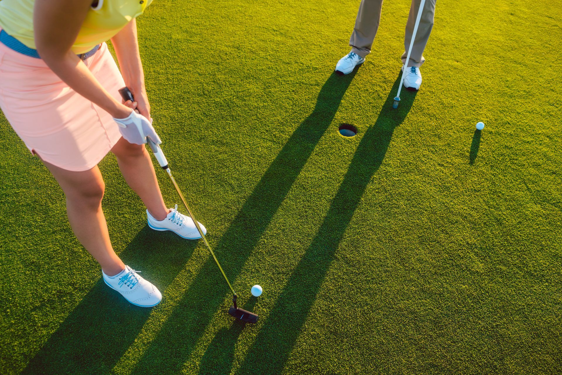 Two golfers putting on a bright green course, with long shadows in the sunlight Two golfers putting on a bright green course, with long shadows in the sunlight