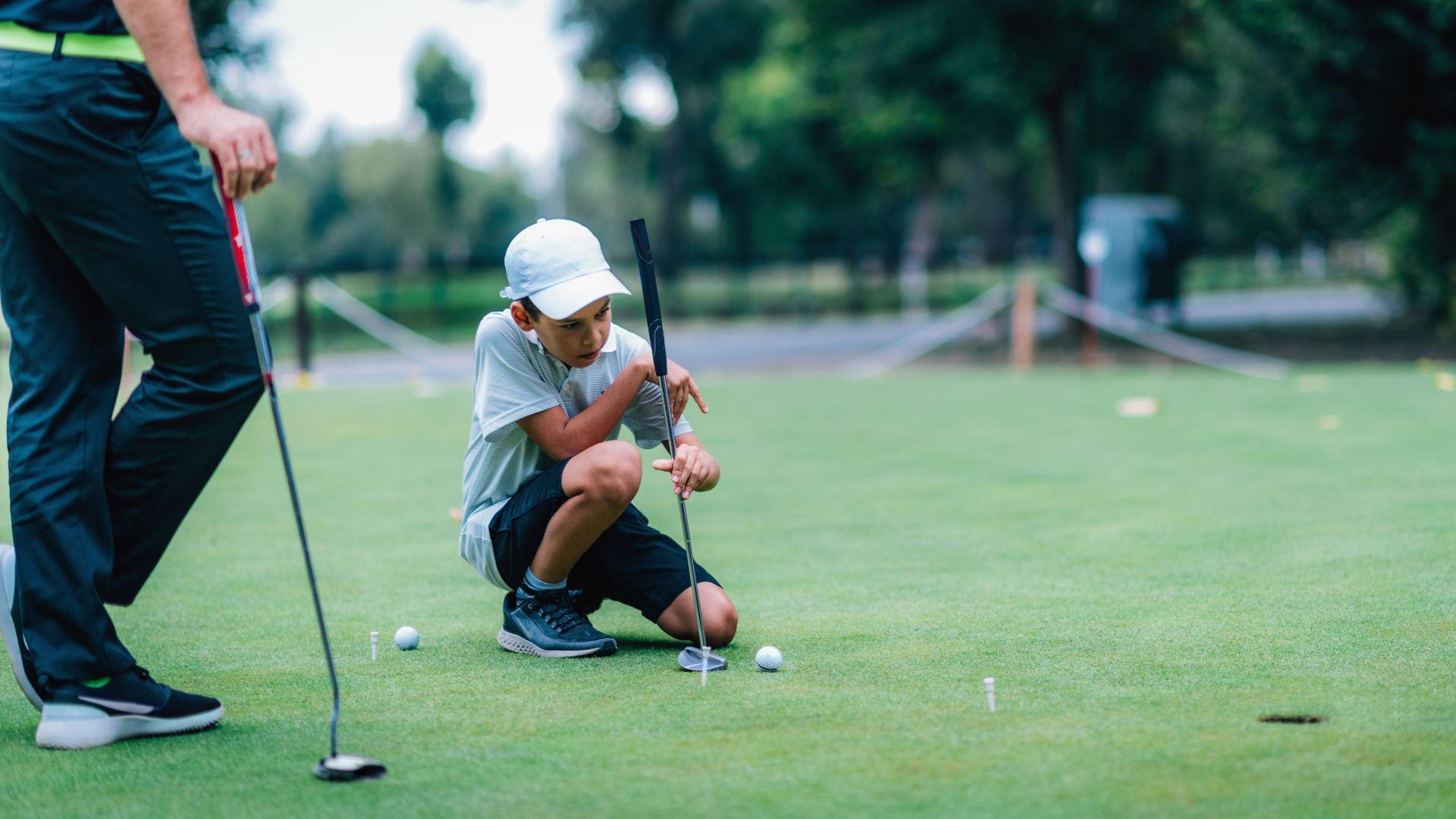 Golfer crouching on a green putting on a golf course beside another golfer holding a putter Golfer crouching on a green putting on a golf course beside another golfer holding a putter